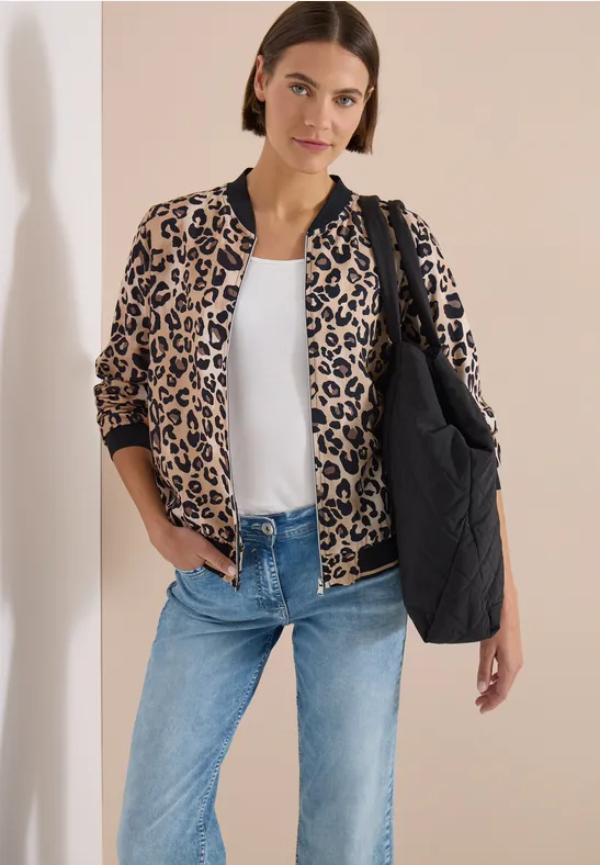 Frau mit Leo-Blouson, weißem Shirt, Jeans und schwarzer gesteppter Tasche vor hellem Hintergrund.
