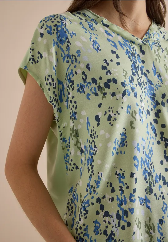 Un chemisier vert clair à motifs abstraits bleu porté par un mannequin.