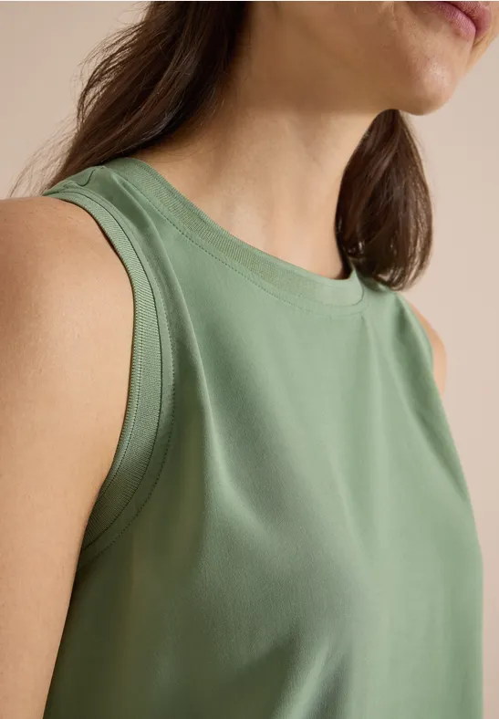 Portrait d'une femme portant un débardeur vert clair sans manches, cadré sur le torse et les épaules.