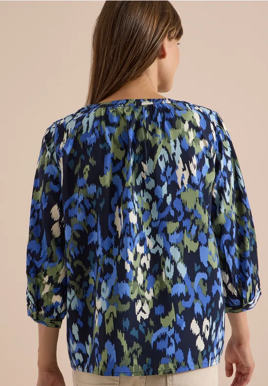 Vue de dos d’une femme portant un chemisier aux motifs abstraits bleus, verts et blancs.
