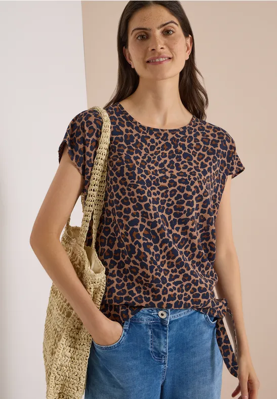 Femme en t-shirt léopard, jean et sac tressé.