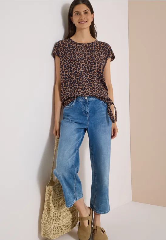 Une femme porte un t-shirt à pois, un jean bleu large, des sandales compensées et tient un sac tressé.