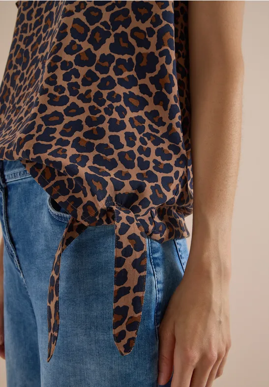 Haut féminin à imprimé léopard avec nœud sur le côté, porté avec un jean bleu.