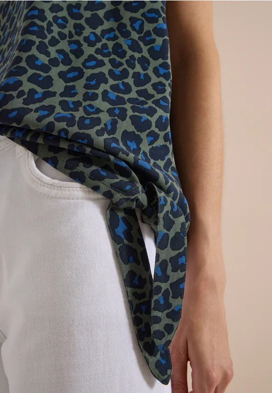 Personne porte un jean blanc et un haut imprimé léopard bleu-vert noué sur le côté.