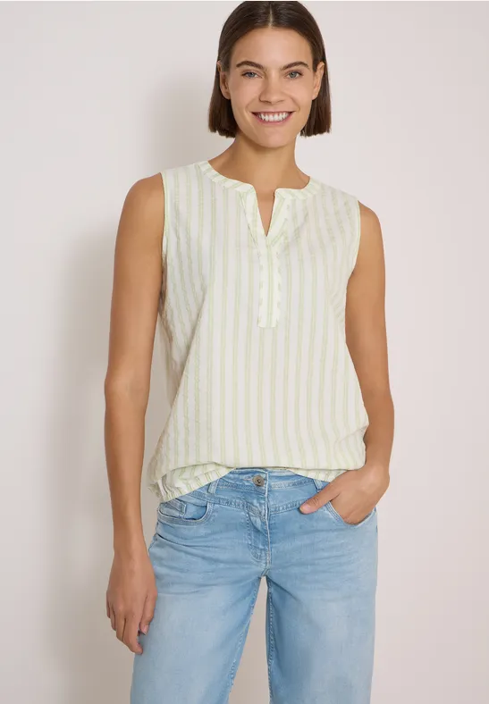 Femme souriante en top sans manches à fines rayures jaunes et jean, posant de manière décontractée.