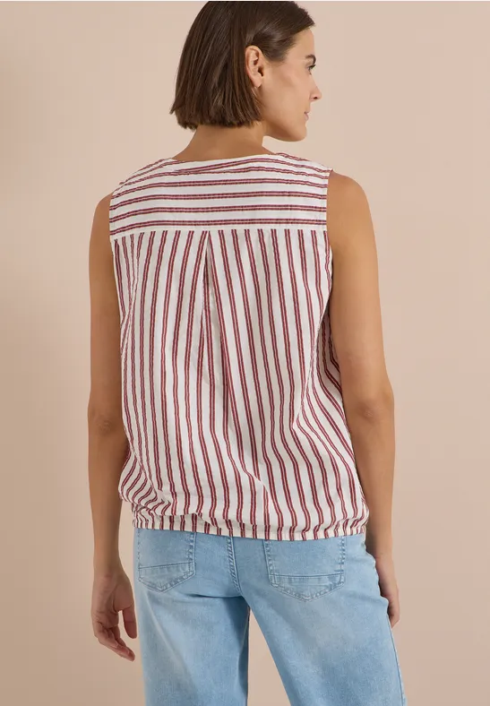 Eine Frau von hinten trägt eine ärmellose Bluse mit roten und weißen Streifen und Jeans.