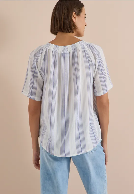 Frau von hinten in einer lockeren, kurzärmligen, weiß-blau gestreiften Bluse mit heller Jeans.