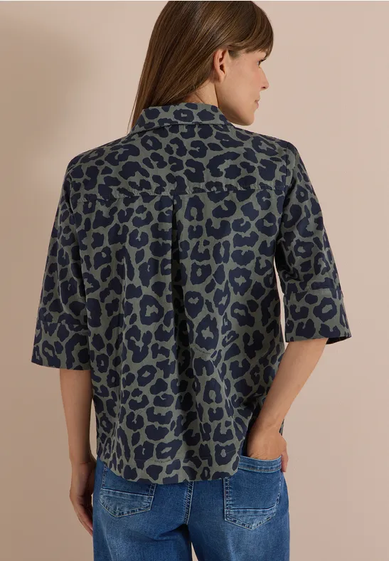 Vue arrière d'une femme portant un chemisier ample à motif léopard et un jean, main dans la poche.