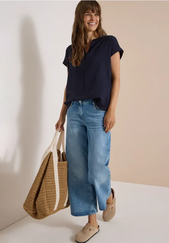 Frau in dunkelblauer Bluse, weiten Jeans, Espadrilles und großem Strohtasche
