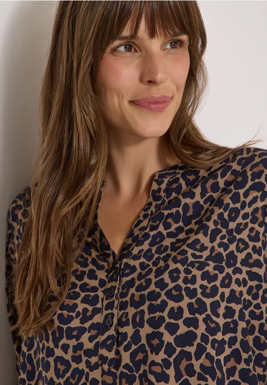 Femme portant une blouse léopard marron et noire, cheveux lâchés, souriante, regard de côté.