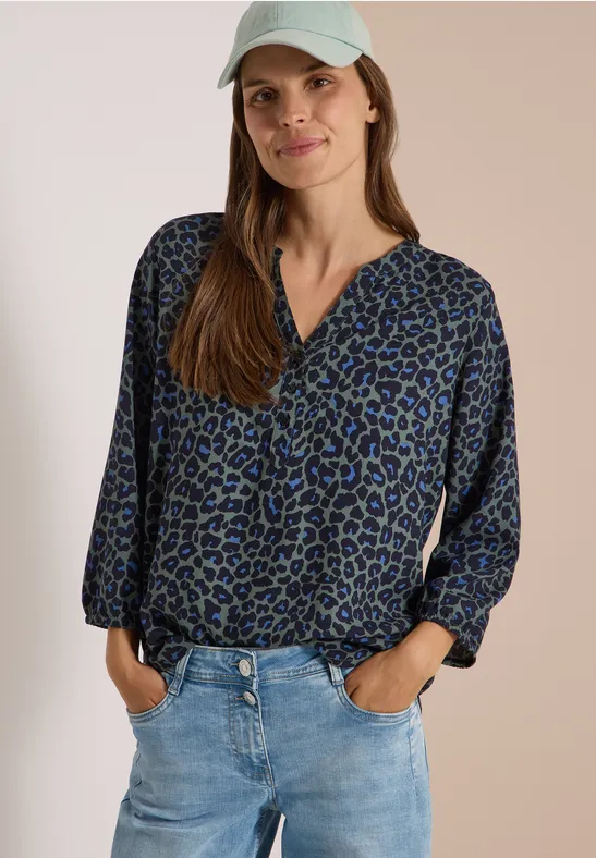 Frau trägt blaue, gemusterte Bluse, Jeans und weiße Kappe