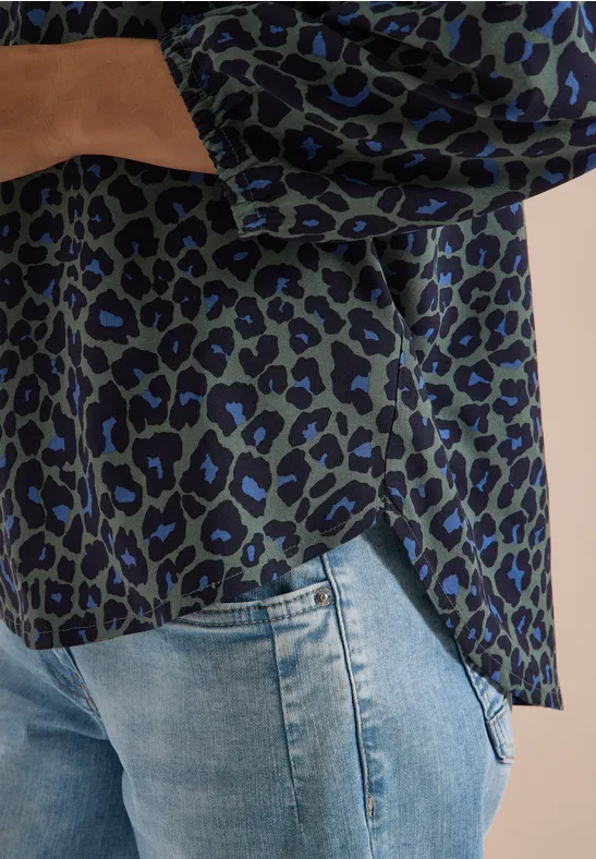 Damenbluse mit grün-schwarz-blauem Leopardenmuster, lässig über hellblaue Jeans kombiniert
