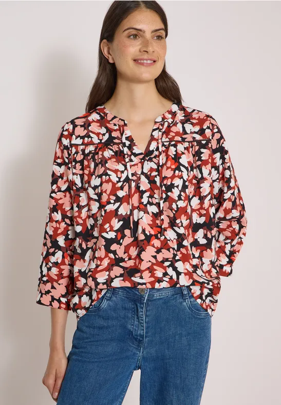 Femme en chemisier à fleurs rouge et noir avec jean bleu.