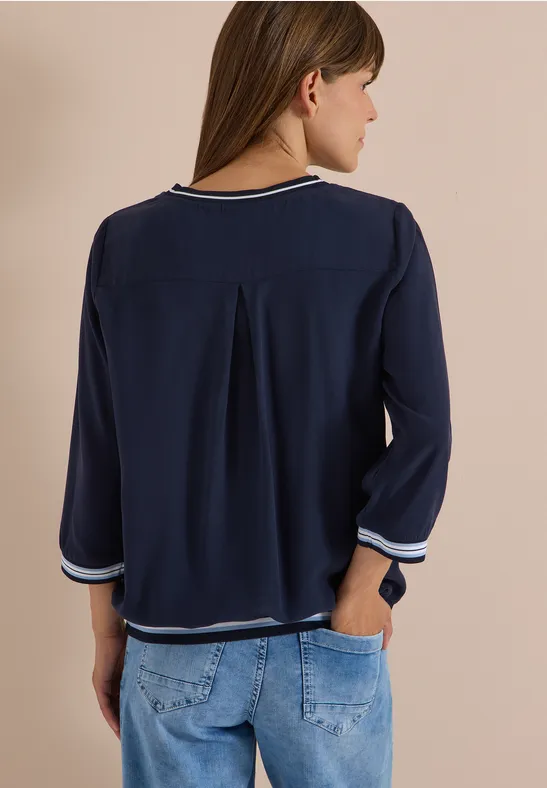 Vue de dos : femme en chemisier bleu marine à manches 3/4 avec bord blanc, associée à un jean.