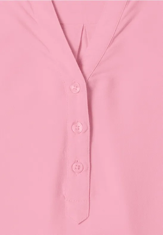 Un haut rose clair à col en V avec trois boutons.