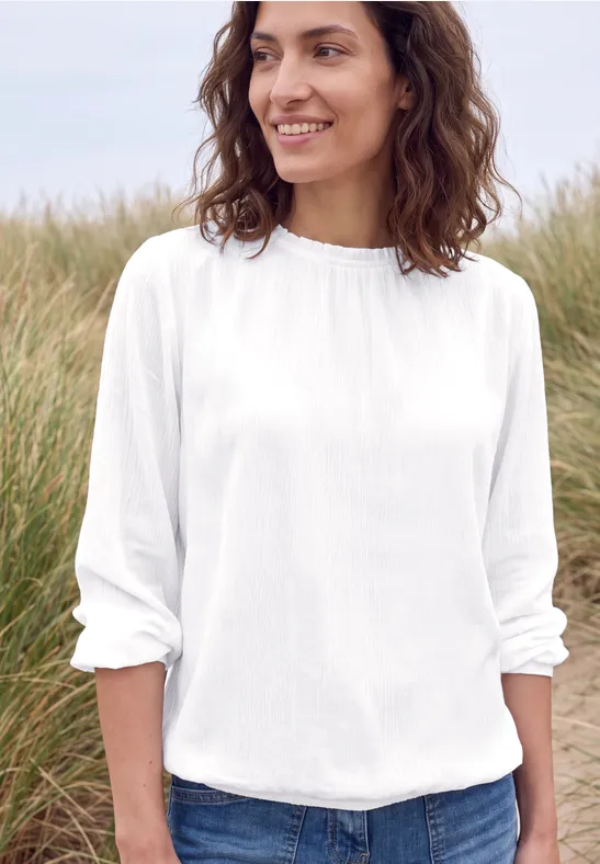 Lächelnde Frau in weißem Langarmshirt vor Strandgras