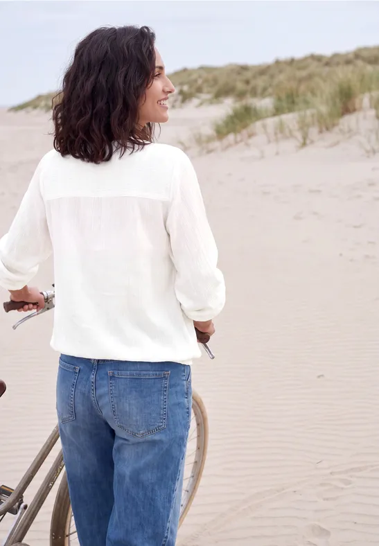 Frau am Strand schiebt ein Fahrrad entlang der Dünen im Sand.