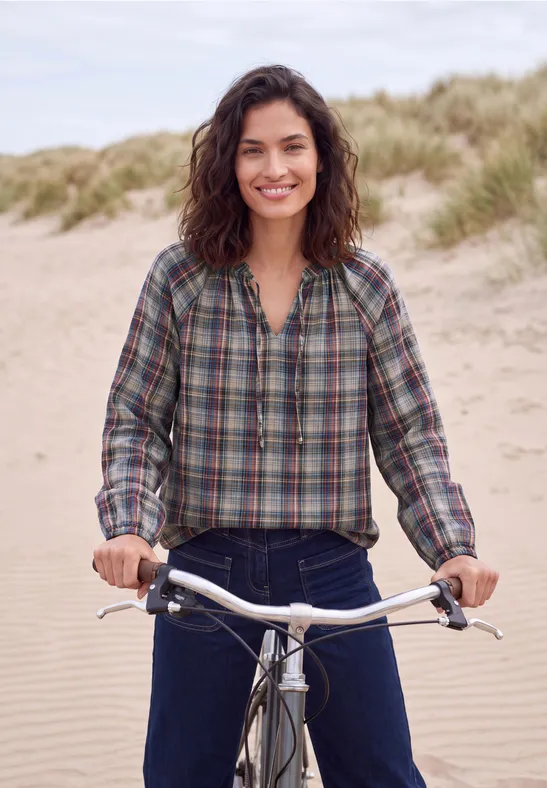 Eine Frau fährt lächelnd Fahrrad am Strand in den Dünen.