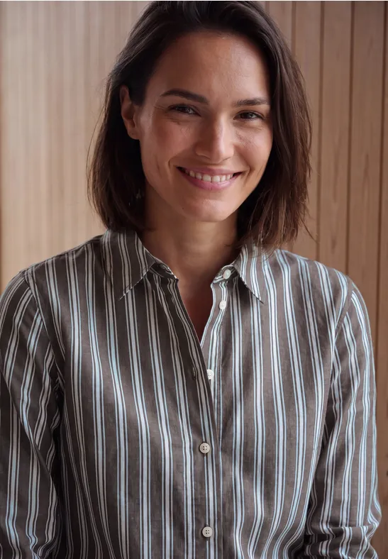 Une femme souriante en chemise rayée devant un panneau de bois.