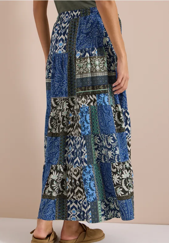 Frau trägt bunten Patchwork-Maxirock in Blau, Schwarz und Weiß mit floralen und geometrischen Mustern.