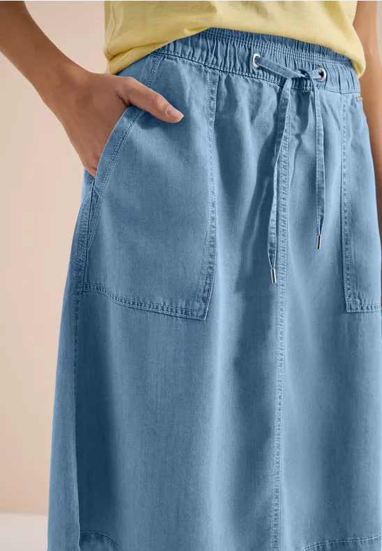 Hellblauer Jeansrock mit elastischem Bund, Tunnelzug und aufgesetzten Taschen, kombiniert mit gelbem Top.