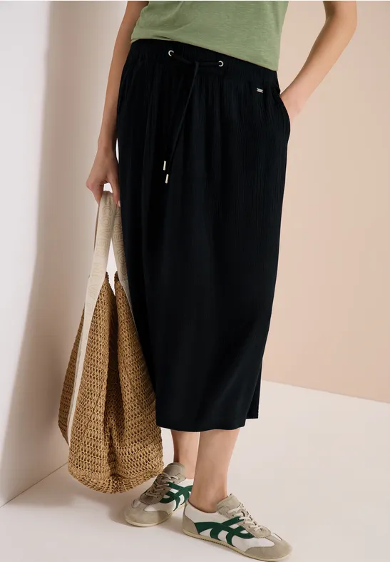 Jupe mi-longue noire, t-shirt vert, baskets blanches, grand sac en paille.