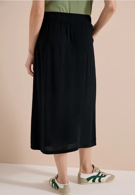 Jupe midi noire portée avec des baskets blanches à touches vertes.