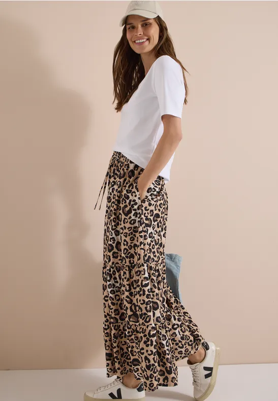 Femme de profil en t-shirt blanc et pantalon large léopard sur fond beige