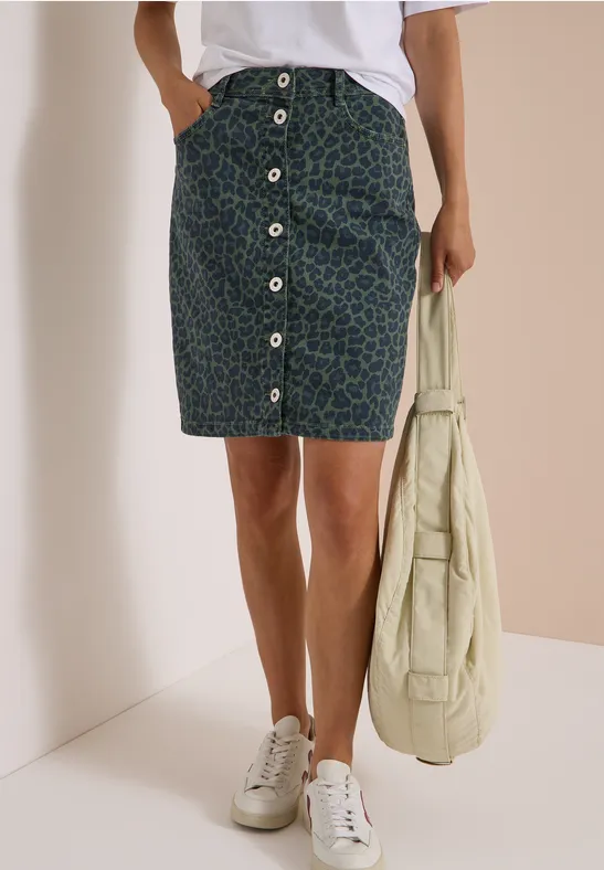 Femme porte une jupe midi boutonnée, baskets blanches et sac fourre-tout beige.