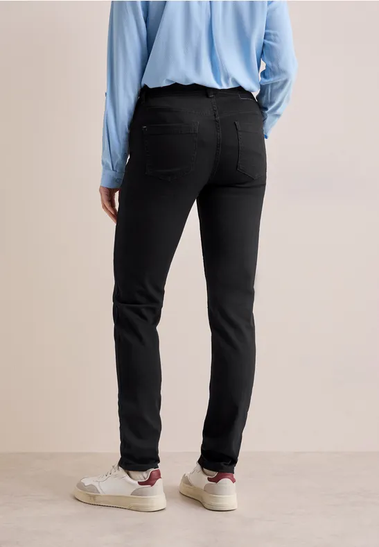 Person in schwarzer Hose, hellblauem Hemd und weißen Sneakers von hinten.