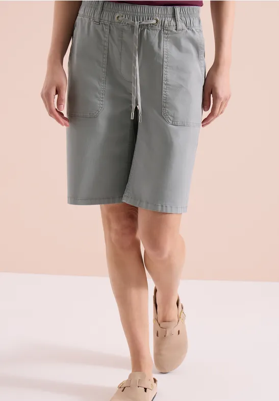 Person in hellgrauen, knielangen Baumwoll-Shorts mit Tunnelzug und Taschen, kombiniert mit beigen Espadrilles.