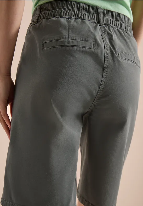 Rückansicht einer Person in olivgrünen Bermudashorts und grünem Top.