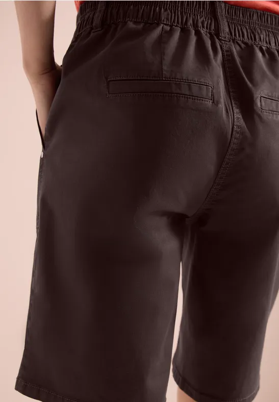 Rückenansicht einer Person in dunklen, knielangen Shorts mit aufgesetzten Gesäßtaschen.