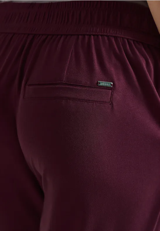 Person in bordeauxfarbenen Jogginghosen mit elastischem Bund und Reißverschlusstasche hinten.