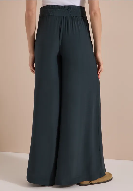 Personne vue de dos portant un pantalon large, fluide et sombre.
