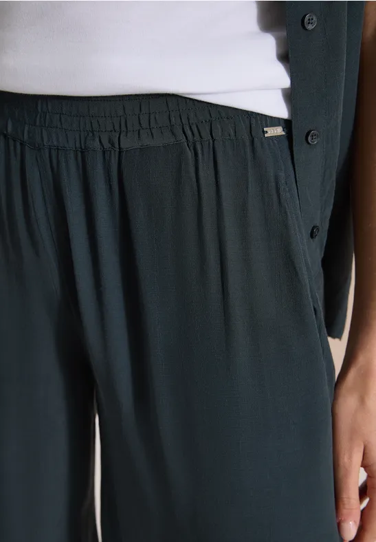 Gros plan: pantalon vert foncé fluide à taille élastique, top blanc et veste vert foncé.