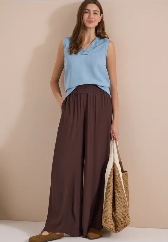 Femme en top sans manches bleu clair, pantalon ample marron et sac en paille