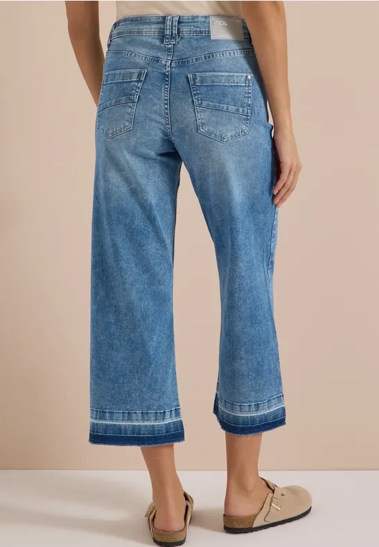 Rückansicht: Person in weiten, knöchellangen Jeans und beigen Loafern.