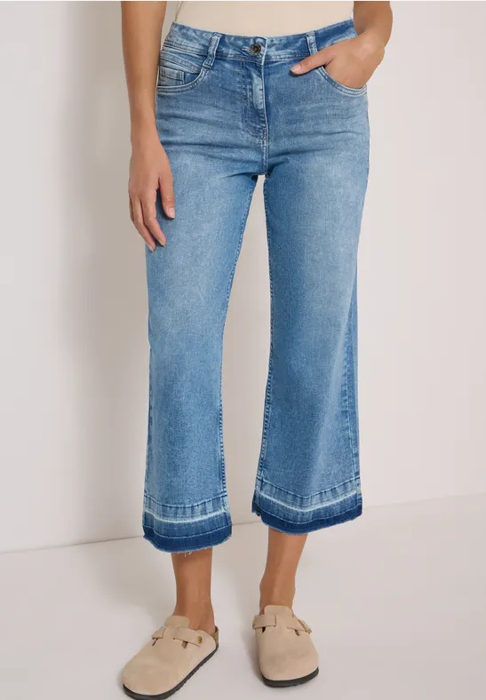 Helle, weit geschnittene Cropped-Jeans mit Umschlag und beigefarbenen Slippern.