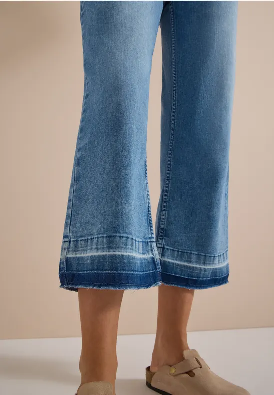 Frau trägt weite blaue Jeans-Culottes mit Ziernähten und beigefarbenen Mules mit Schnalle.