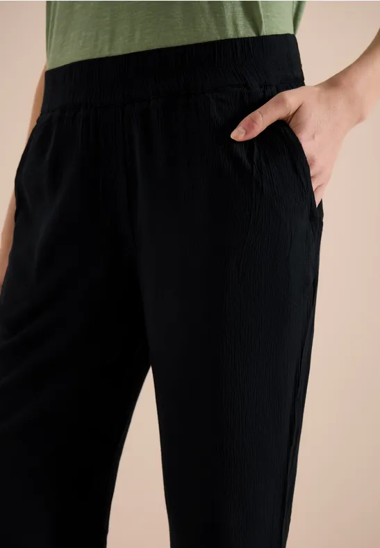 Schwarze, lässige Hose mit elastischem Bund und seitlicher Tasche, Hand in Tasche