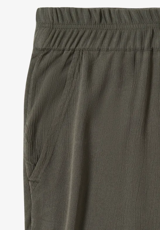 Detail einer olivgrünen Stoffhose mit elastischem Bund und seitlicher Tasche in leicht strukturierter Optik.