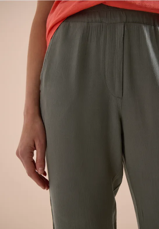 Nahaufnahme einer Person in olivgrünen Hosen mit Gummibund und einem korallfarbenen Oberteil.