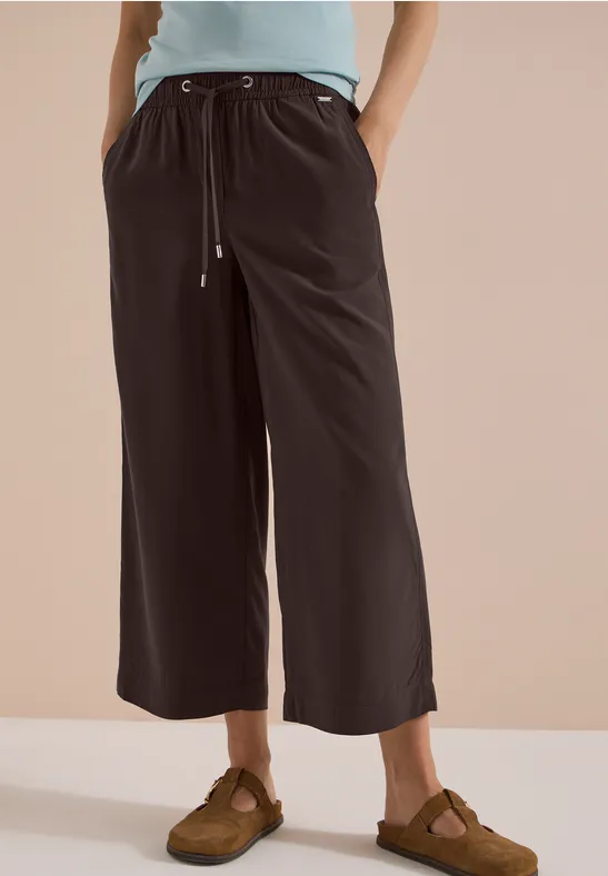 Schwarze, weite Culotte-Hose mit Kordelzug, kombiniert mit Sandalen.