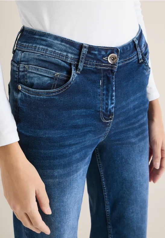 Blick auf eine Person in dunkelblauen Jeans und weißem Oberteil, Hand an der Hüfte.