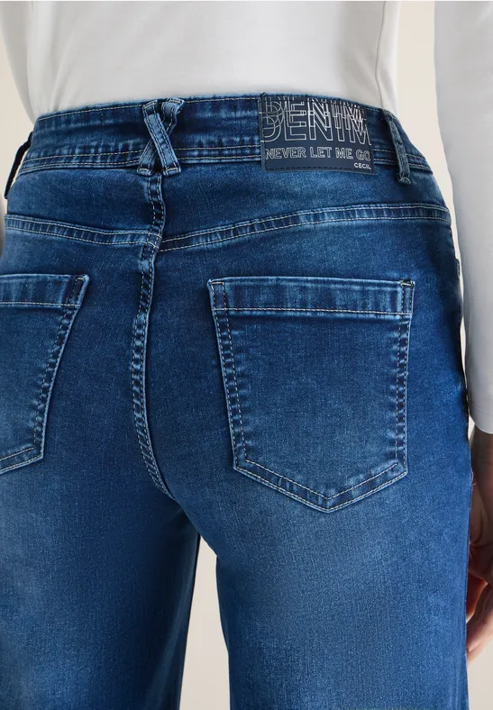 Damenjeans in dunkler Waschung, zwei aufgesetzte Gesäßtaschen, eng anliegend, mit weißem Top.
