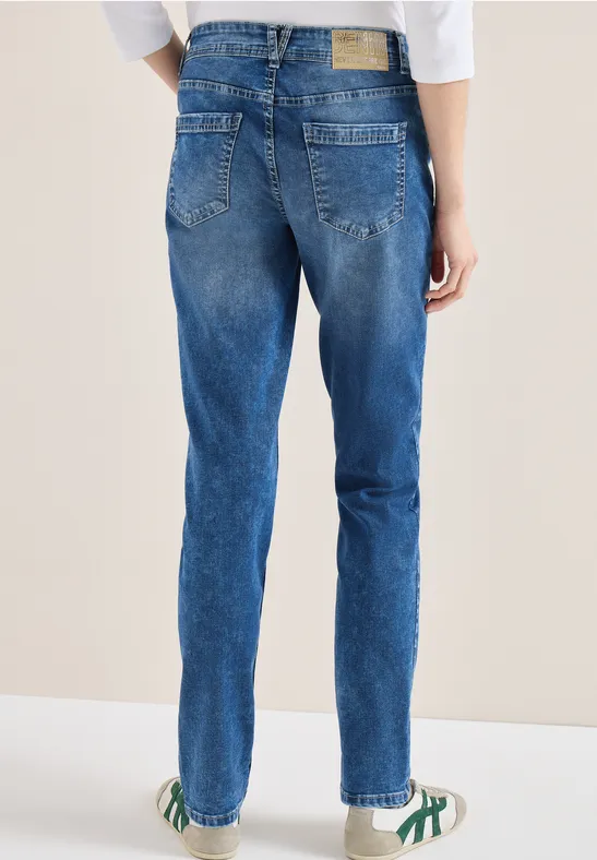 Person von hinten in blauen Jeans und weißen Sneakers mit grünen Details.