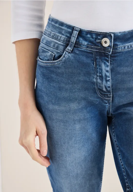 Damenoberkörper mit enger blauer Jeans und weißem Oberteil, Hand locker am Bein.