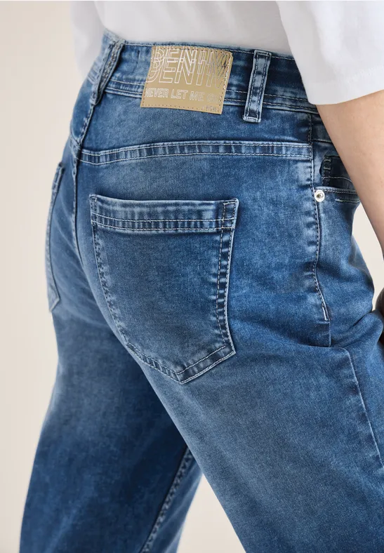 Nahaufnahme von blauen Jeans mit Gesäßtaschen und Label, darüber weißes Oberteil.
