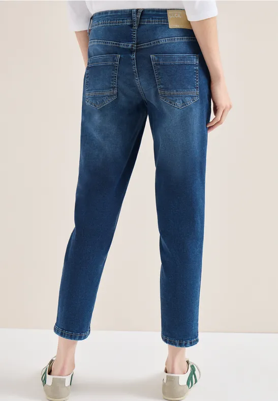 Vue arrière d’une personne portant un jean bleu foncé et des baskets blanches à détails verts.